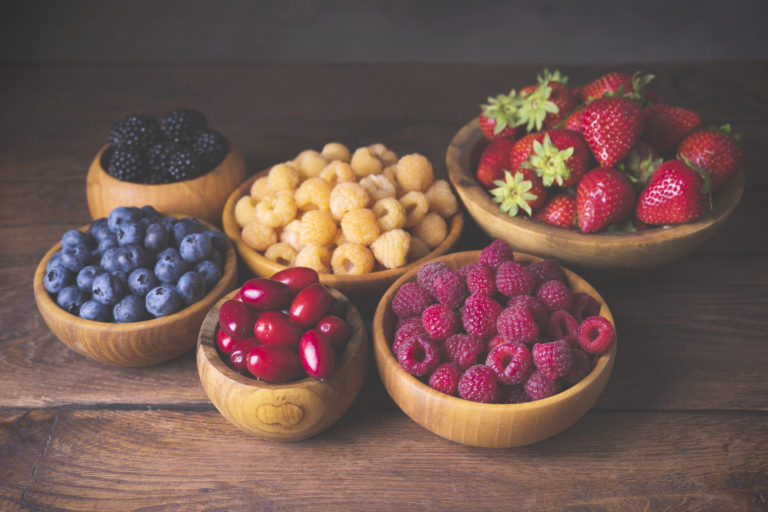 Blackberry, strawberry, yellow and red raspberries, dogwood in wooden bowls on a dark wooden old background in vintage style.